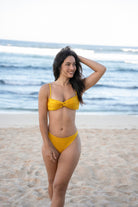 Bikini model in a mustard yellow gold bandeau bikini top with front & back cut-outs & a high-waisted high-rise cheeky bottom.