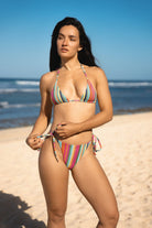 Woman in a string bikini with triangle top and tie-side cheeky bikini bottoms on the beach.